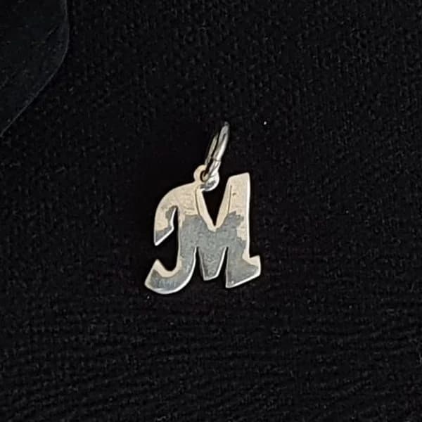 Dije silueta con la letra “M”